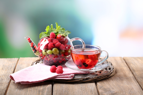 Fruit red tea with wild berries in glass cup, on wooden table, on bright background