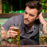 Lonely man in bar. Depressed young man drinking beer and holding hand in hair while sitting in bar