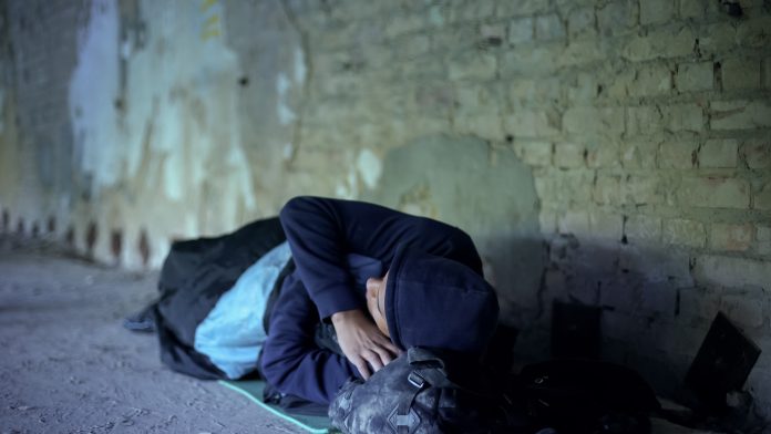 Homeless young man sleeping on street, indifferent egoistic society, poverty