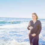 pregnant woman in dark blue dress touching her belly with love and care walking and on the beach.