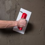 Hand holding a spatula with construction mix and smoothes out bumps