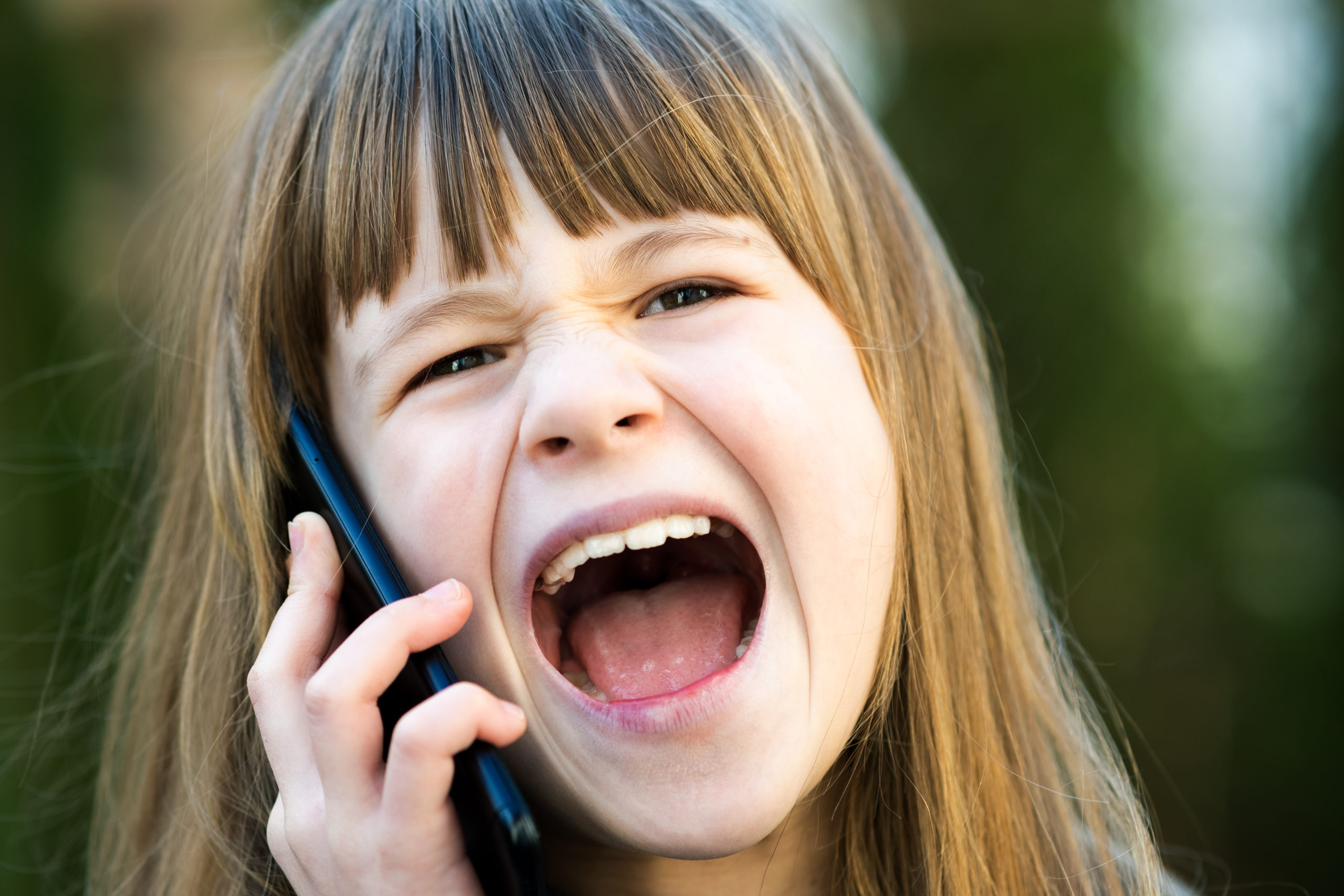 Portrait of angry child girl with long hair talking on cell phone. Little female kid having discussion on smartphone. Children communication concept.