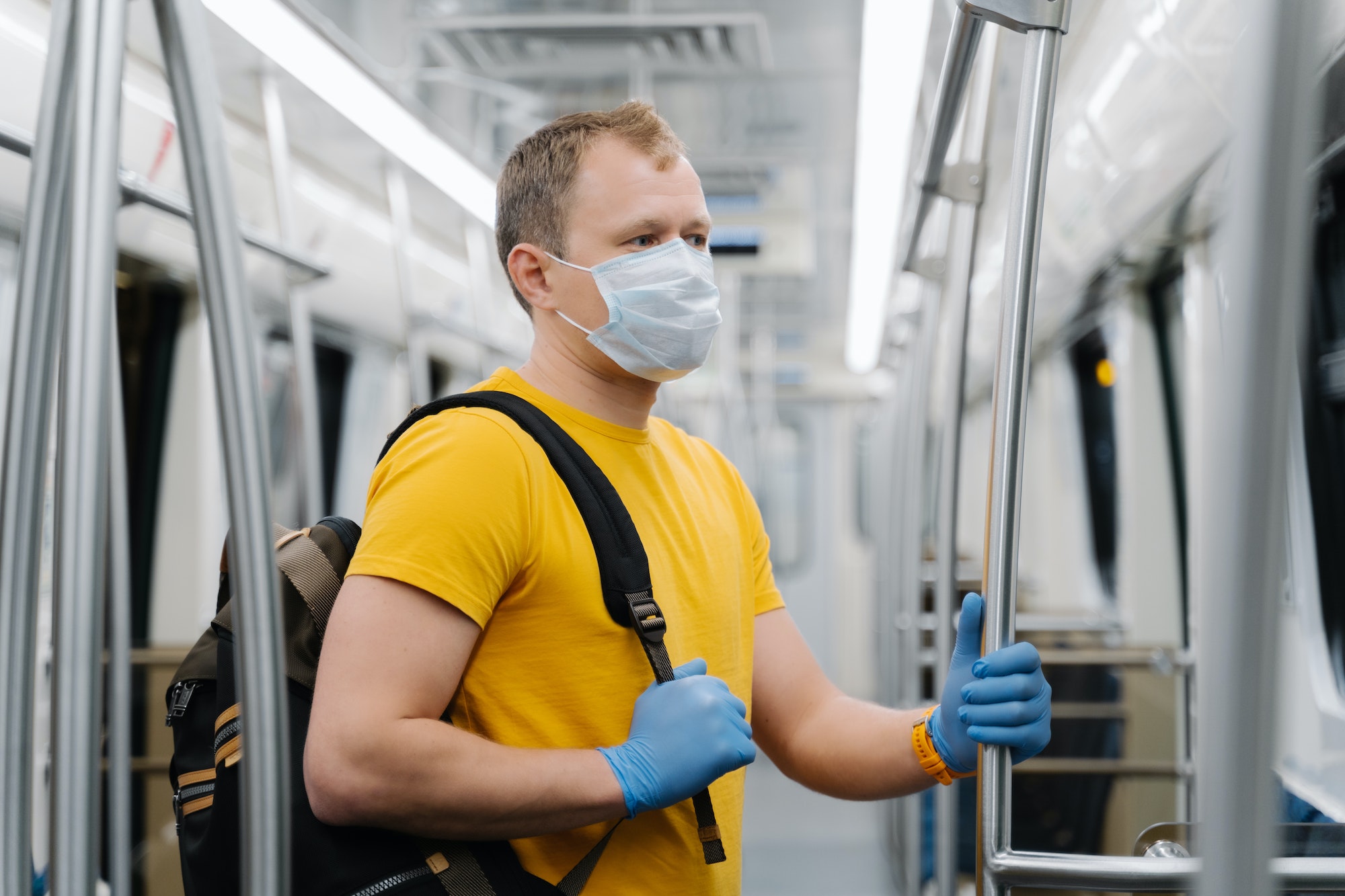 European man wears surgical mask, commutes in metro or underground, carries backpack