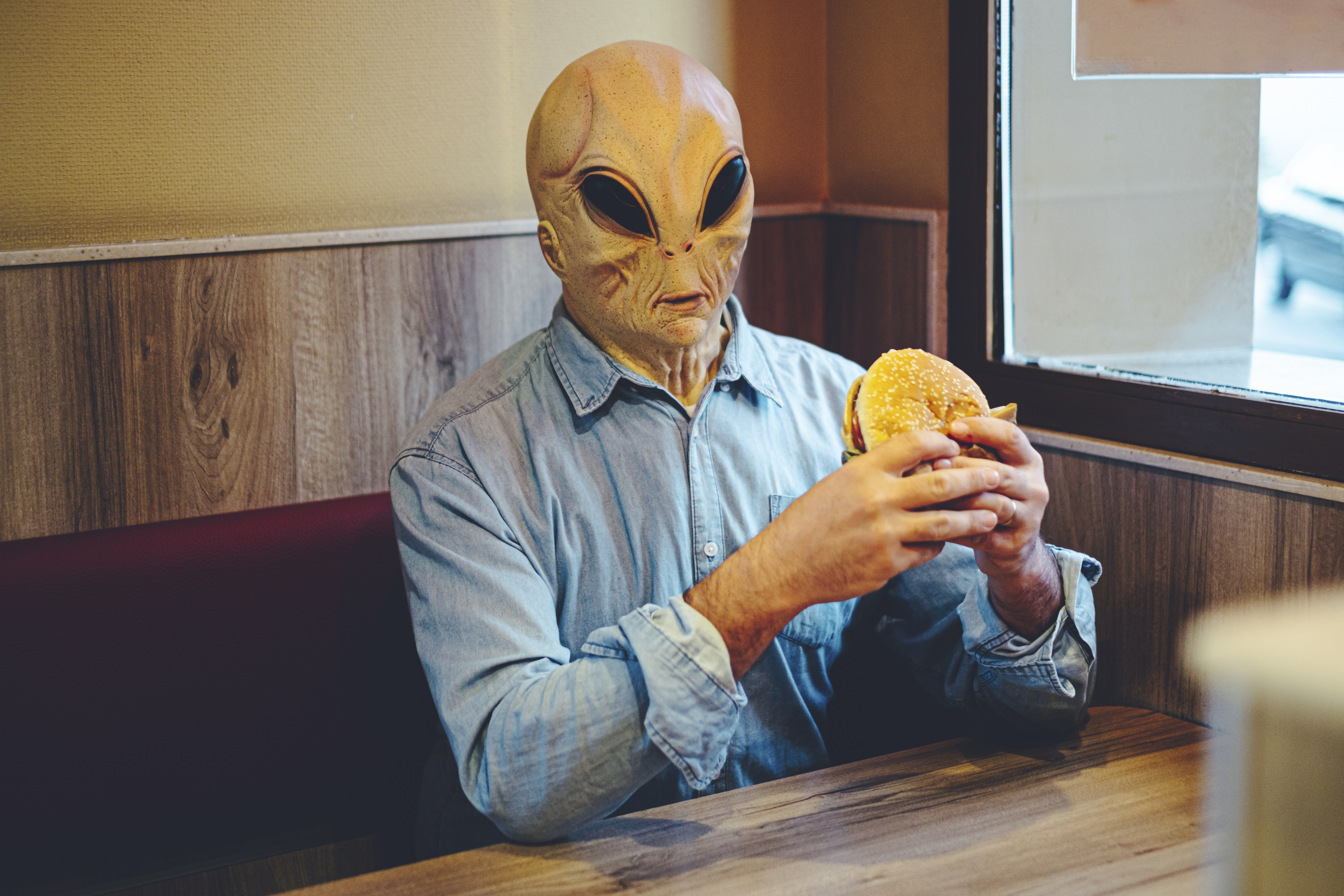 Extraterrestrial ufo alien eating an hamburger at the fast food sitting alone at the table